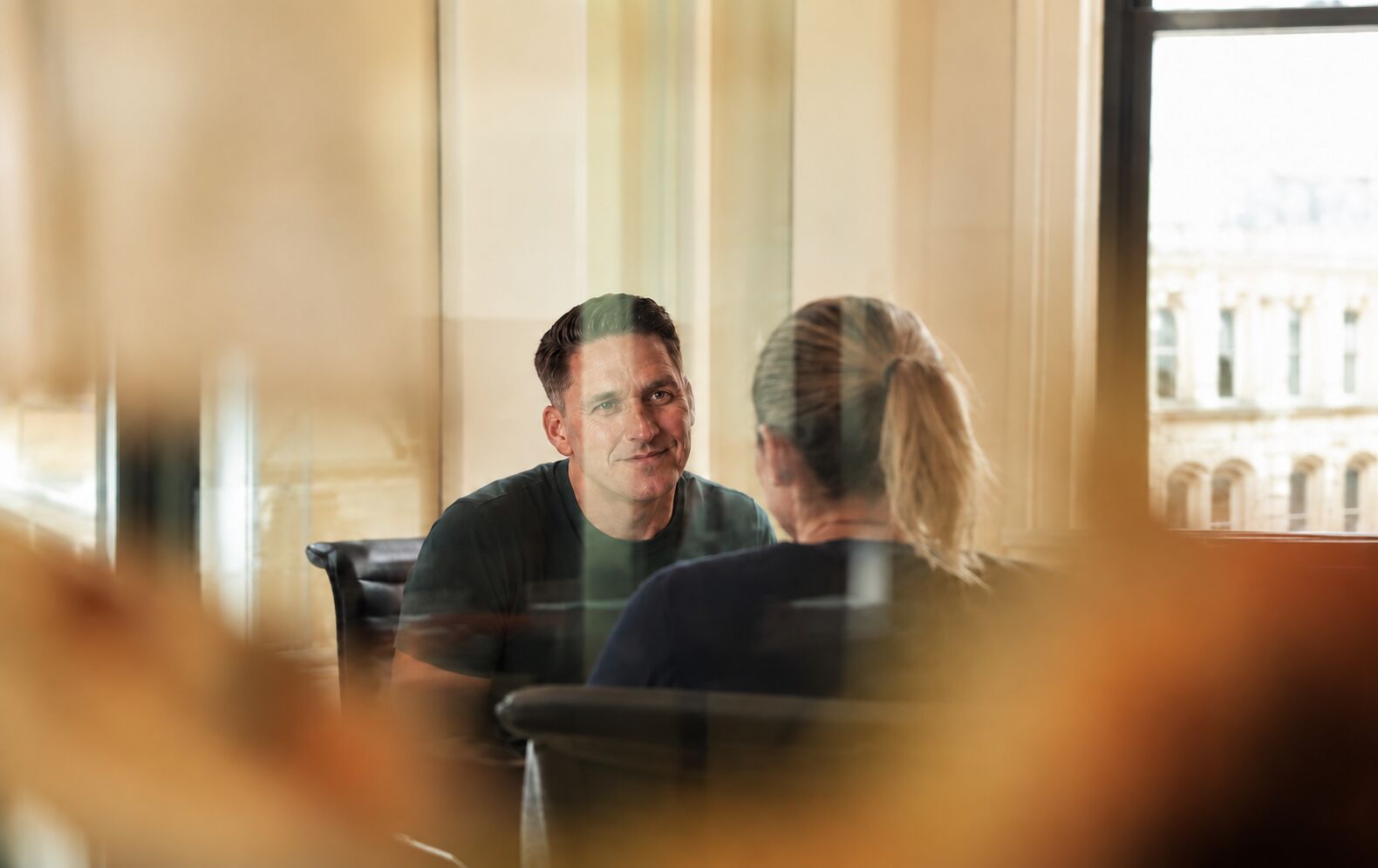 Two people in conversation, framed through soft foreground blur