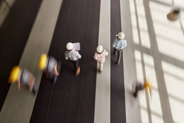 People crossing a sunlit concourse, seen from above