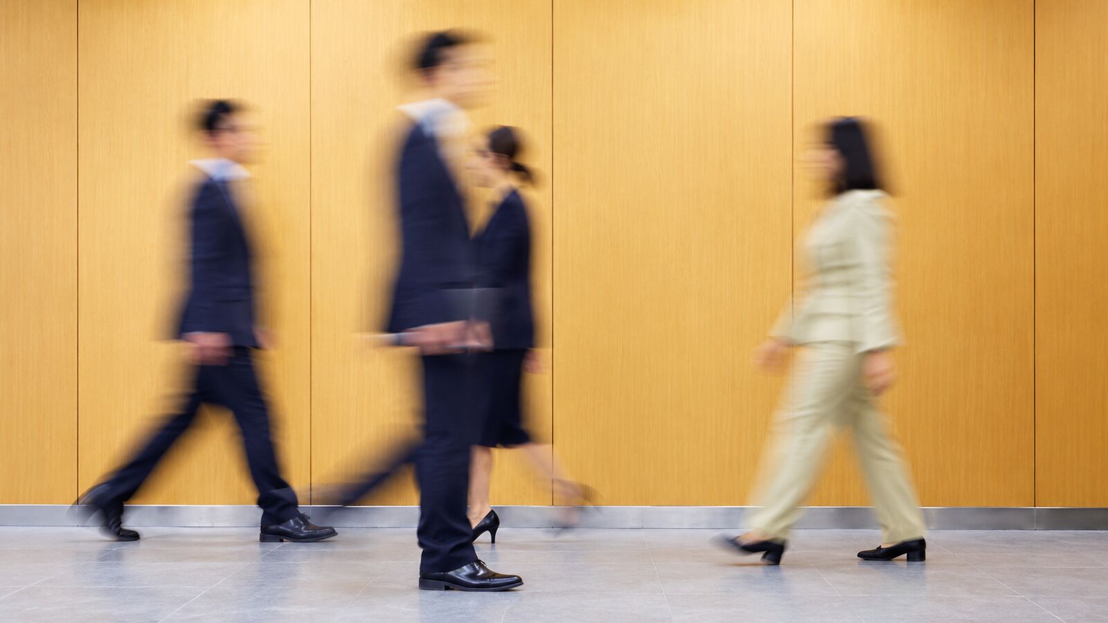 People walking past a warm wall, softened by motion blur