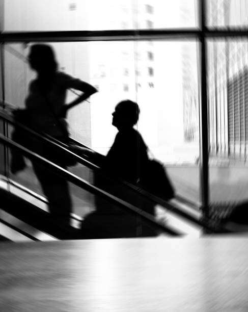 Silhouettes on an escalator against tall windows