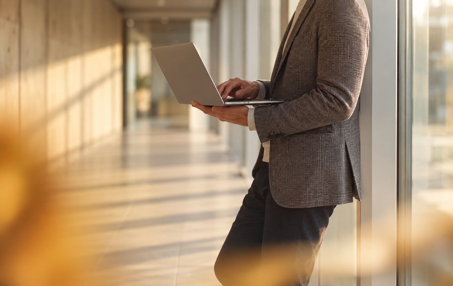 A person holding a laptop in a sunlit corridor